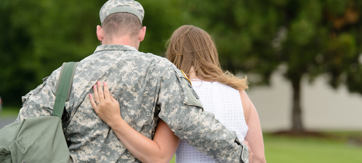 Close-up of a servicemember and his wife, walking hand in hand. A sign advising "Free Help. Don't pay a fee for student loan services." is near the photo.